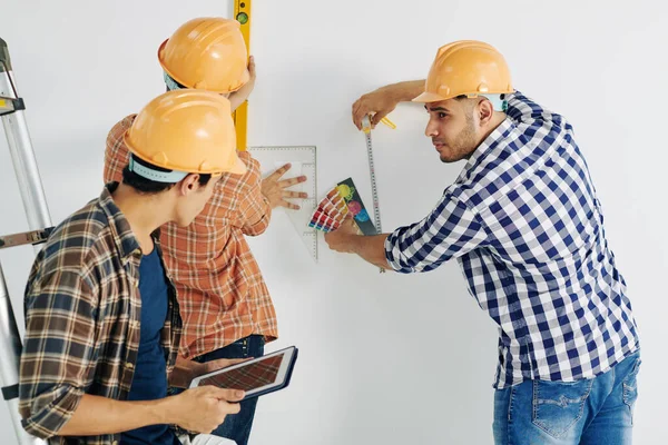 さらなる作業のために測定を取るチェックシャツと黄色のハード帽子を身に着けている3人の現代の手動労働者のグループ — ストック写真