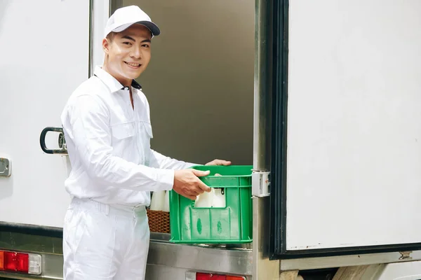 亚洲送奶员身穿白色衣服 把装有奶瓶的塑料盒放进货车 看着相机 复制空间的横向中等照像 — 图库照片