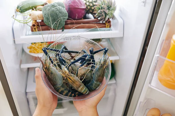 人类的手从冰箱里拿着装有新鲜蓝色带刺龙虾的玻璃碗 — 图库照片