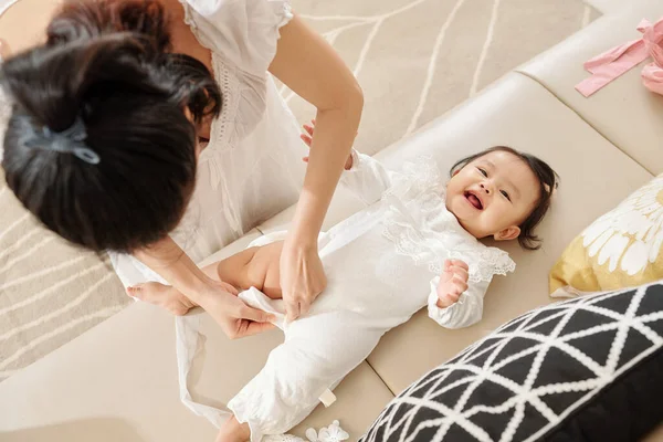Genç Anne Sevimli Gülümseyen Bebeğine Beyaz Bir Vücut Giydiriyor — Stok fotoğraf