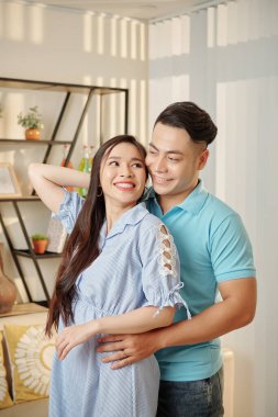 Mutlu yakışıklı Asyalı adam güzel kız arkadaşına arkadan sarılıyor.