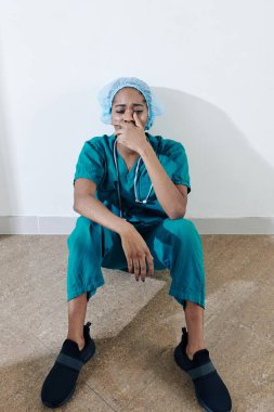 Ameliyatta hastasını kaybettikten sonra ofis koridorunda yerde oturan yorgun genç hemşire.