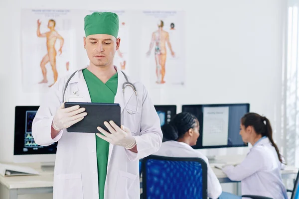 의사가 태블릿 컴퓨터로 환자의 병력을 읽으면서 동료들은 업무용 달력을 배경으로 — 스톡 사진