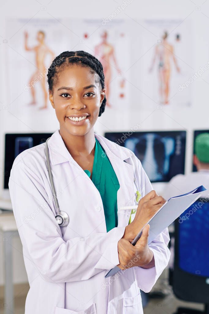 Portrait of beautiful young general practitioner smiling at camera when filling document