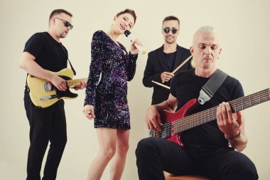 Orkestrası arka planda şarkı söylerken orta yaşlı şık bir adam bas gitar çalıyor.