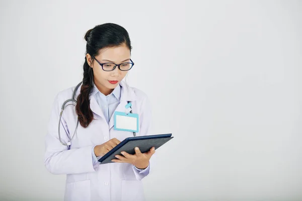 Young Asian medical intern checking information on tablet computer, isolated on white