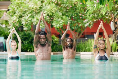 Ciddi genç erkek ve kadınlar yüzme havuzunda ağaç yogasında dururlar.