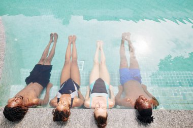 Bir grup genç erkek ve kadın yüzme havuzunda dinleniyor, gün ışığının ve ferahlatıcı suyun tadını çıkarıyorlar.