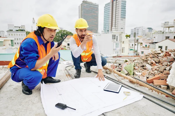 Inżynier Budowlany Wskazujący Ścianę Budynku Kiedy Wykonawca Używa Krótkofalówki Aby — Zdjęcie stockowe
