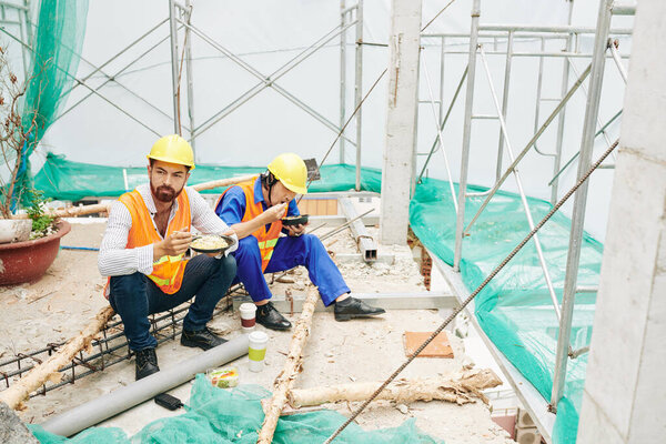 Engineer and builder having lunch at construction site, eating noodles, salad and coffee