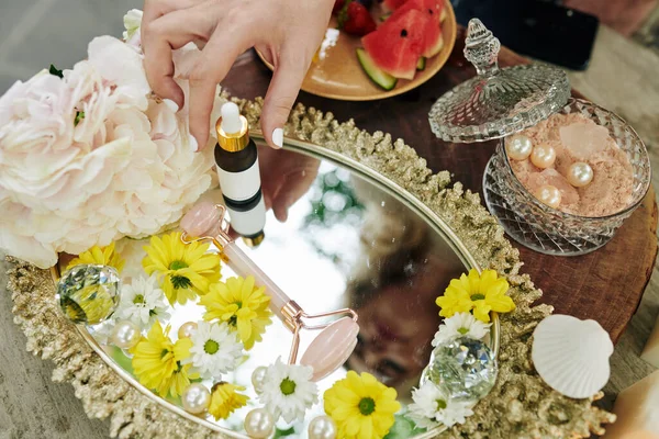 ローズクオーツマッサージオイルと花と金属トレイにエッセンシャルオイルの小さなボトルを置く女性 — ストック写真