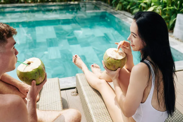 一对快乐的年轻夫妇在温泉酒店的游泳池边休息时享受椰子鸡尾酒 — 图库照片