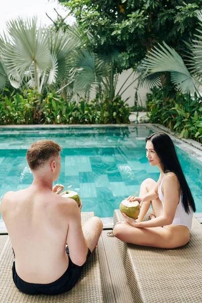 若い男と女性がシャイに座って スイミングプールでラウンジ さわやかなココナッツ水を飲んでチャット — ストック写真