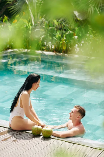 一个笑着摸女朋友腿的年轻人坐在游泳池边 劝她去游泳 — 图库照片