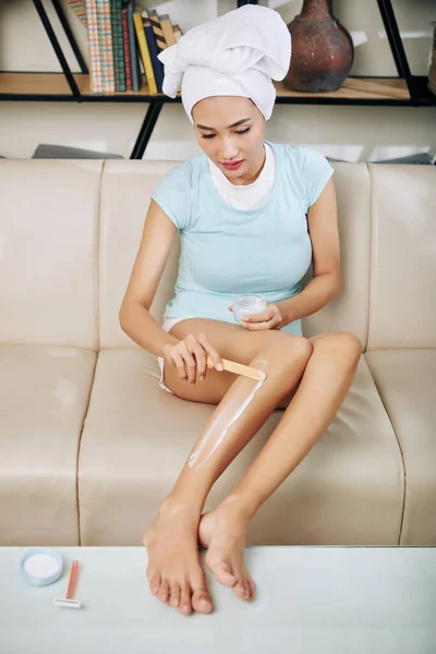 若い女性は髪を削除する木製のへらで足に脱毛クリームを適用します — ストック写真