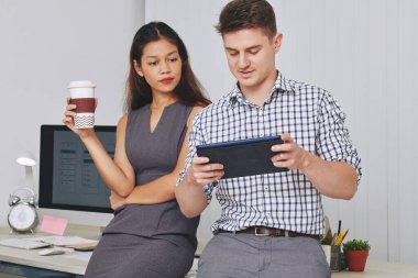 Kahve içen ve meslektaşının elindeki tablet bilgisayardan ekrana bakan oldukça genç, melez bir iş kadını.