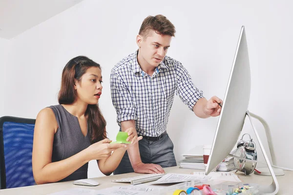 UI designer pointing at computer screen when his colleague sticking note with important note