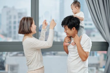 Neşeli genç Asyalı çift evde yeni doğmuş bebekle eğleniyor.