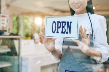 Gülümseyen genç garson, cam kapısına açık tabela yapıştırıyor.