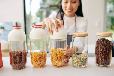 Gülümseyen Vietnamlı garson müşteriye kahvaltı hazırlamak için mısır gevreğiyle konteynır açıyor.