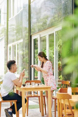 Güzel Vietnamlı genç bir kadın kafeterya masasına eğilip blogu için kahvaltı fotoğrafı çekiyor.
