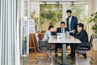 İş ekibi toplantıda gelişme stratejisini tartışıyor, fikirleri paylaşıyor ve raporları kontrol ediyor