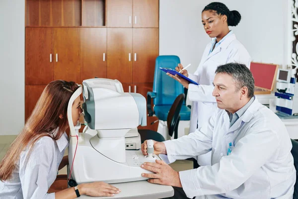 助理填写医疗文件时 严重眼科医生检查妇女的视力 — 图库照片