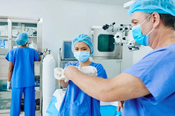 Jovem Assistente Ajudando Cirurgião Colocar Luvas Cirúrgicas Esterilizadas Sala Cirurgia — Fotografia de Stock