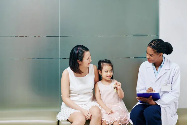 微笑着友善的年轻黑人儿科医生与小女孩和她的母亲交谈 — 图库照片