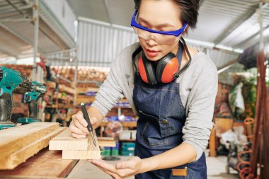 Korumalı gözlüklü profesyonel kadın marangoz kesmeden önce tahta tahtaya izler çiziyor.