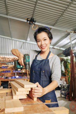 Kot önlüklü gülümseyen Asyalı kadın marangoz portresi atölyedeki tezgahta marangozluk yapıyor.