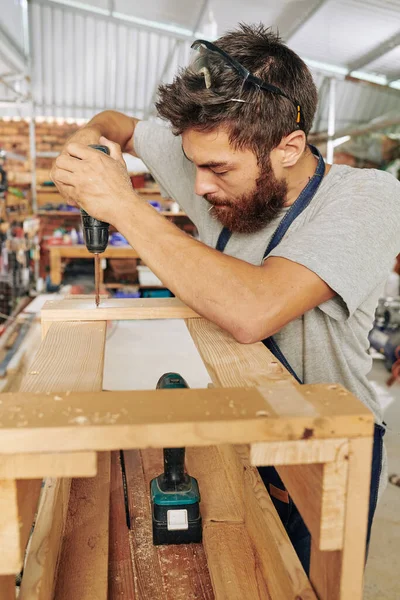 木製のスツールに若い大工の運転ネジを集中 — ストック写真