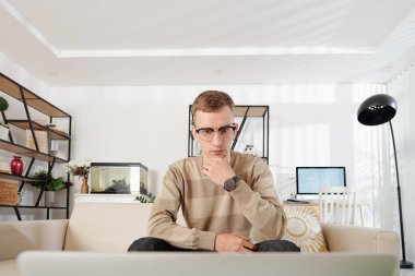Kapatma nedeniyle evden çalışırken gözlüklü genç adam bilgisayar ekranında yazı ya da e-posta okuyor