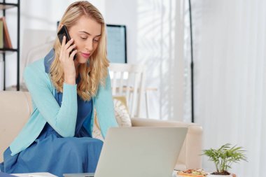 Güzel genç bir kadın dizüstü bilgisayarından e-posta okuyor ve evden çıkarken telefonla konuşuyor.