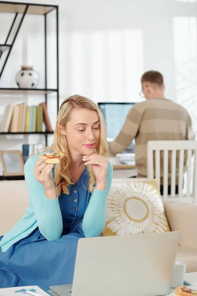 Fiatal Eszik Pizza Ellenőrzi Maileket Amikor Férje Dolgozik Számítógép Háttérben — Stock Fotó