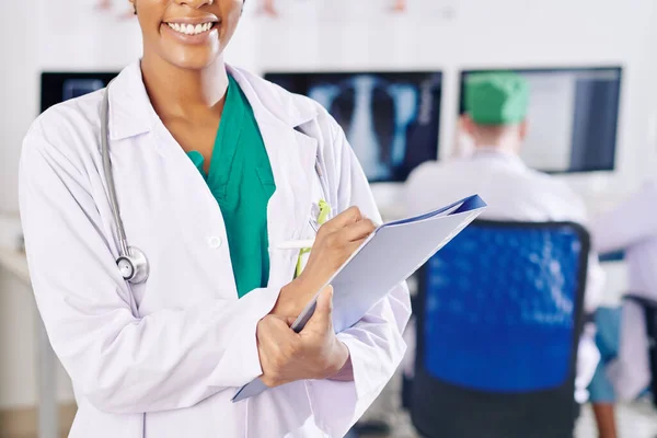 Cropped image of Black female physician with beautiful toothy smiling filling document in her hands