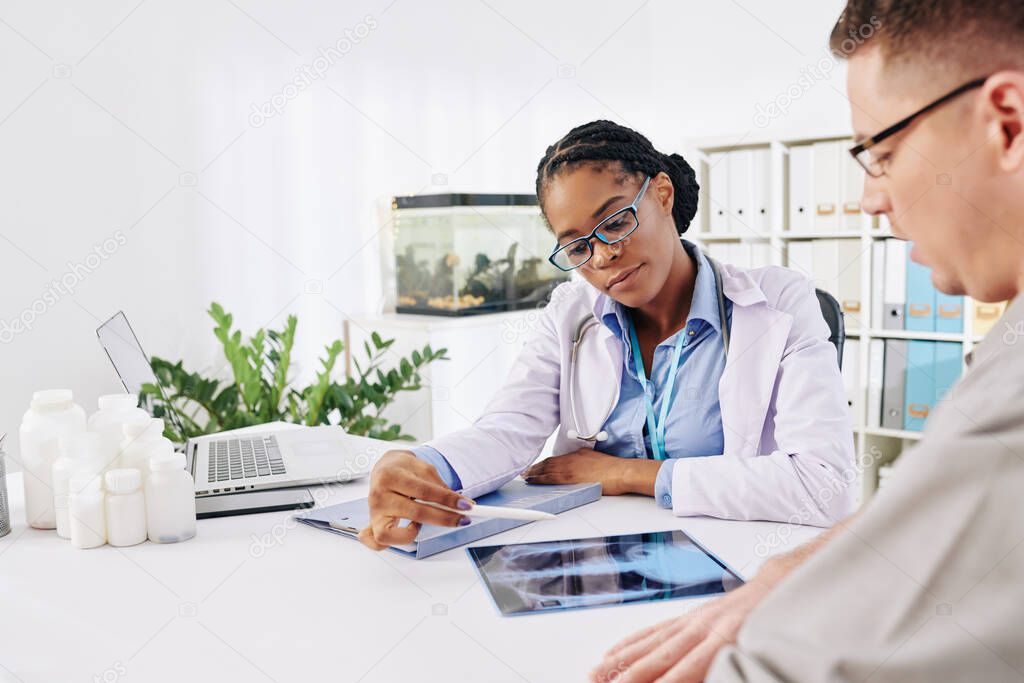 Black female general practitioner discussing lungs x-ray with patient with suspected tumor