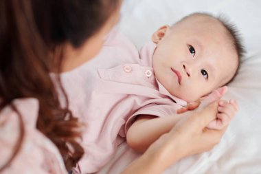 Anne, gülümseyen küçük bebeğinin eline dokunuyor.