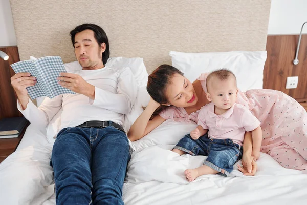 Young Vietnamese Man Lying Bed Reading Book His Wife Playing — Stock Photo, Image