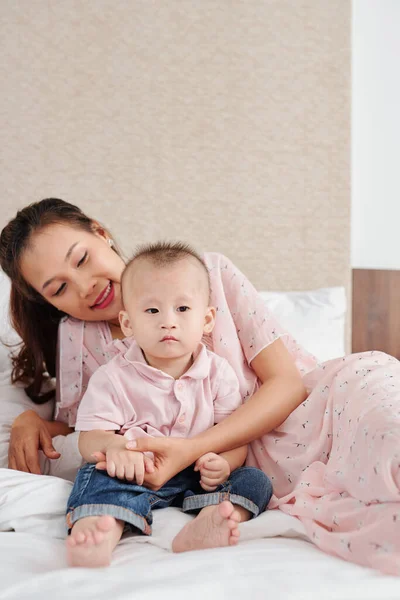 年轻的越南妇女牵着小儿子的手 在卧室里躺在床上 脸上挂着迷人的笑容 — 图库照片