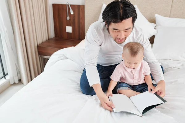 Mężczyzna Siedzący Łóżku Swoim Synkiem Czytający Ciekawą Książkę Podczas Pobytu — Zdjęcie stockowe