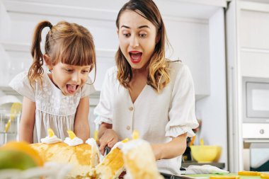 Heyecanlı genç kadın ve küçük kızı evde pişirdikleri mandalina dolgusu ile İsviçre böreği kesiyorlar.