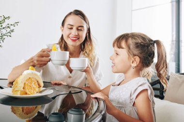 Mutlu anne ve kız çay içip, portakal dolması ve krema ile lezzetli pastalar yiyorlar.