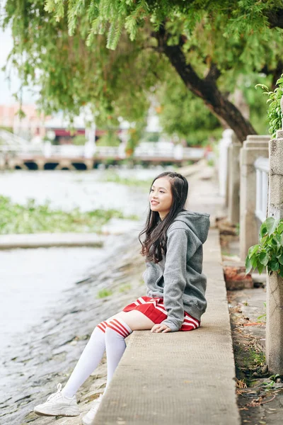 Lächelnde Junge Asiatin Rock Kapuzenpulli Und Schenkelhohen Socken Sitzt Flussufer — Stockfoto