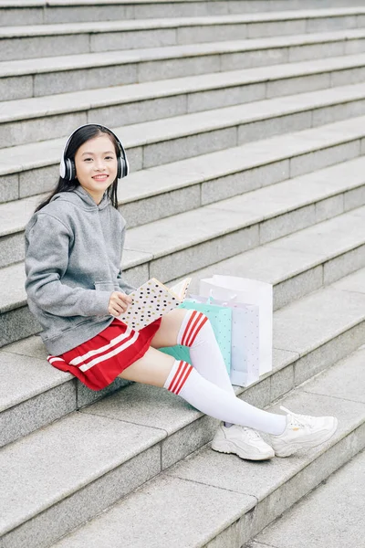Usmívající Veselá Asijská Dívka Odpočívající Schodech Nakupování Čtení Knihy Poslechu — Stock fotografie