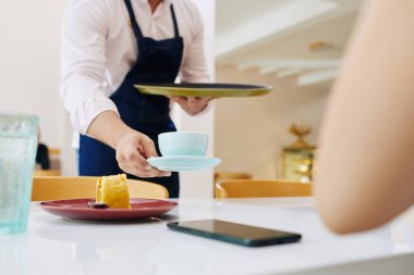 Garsonun kadın müşterinin önüne tatlı ve kahve koyarkenki görüntüsü.