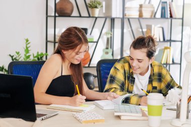 Gülümseyen gençler evde ödev yaparken öğrenci defterlerini kontrol ediyorlar, makale yazıyorlar ya da denklemleri çözüyorlar.
