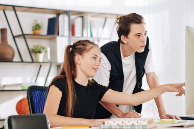 Heyecanlı genç kız bilgisayardaki projesini kardeşine ya da arkadaşına gösteriyor.