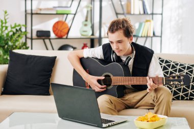 Genç çocuk tablet bilgisayarda webinar izleyip gitar çalmayı öğrenmeye çalışıyor.