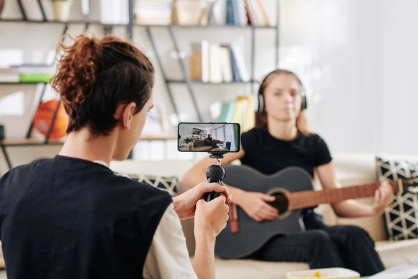 在拍摄他的朋友弹奏吉他和为一些比赛唱歌时 十几岁男孩用智能手机 — 图库照片